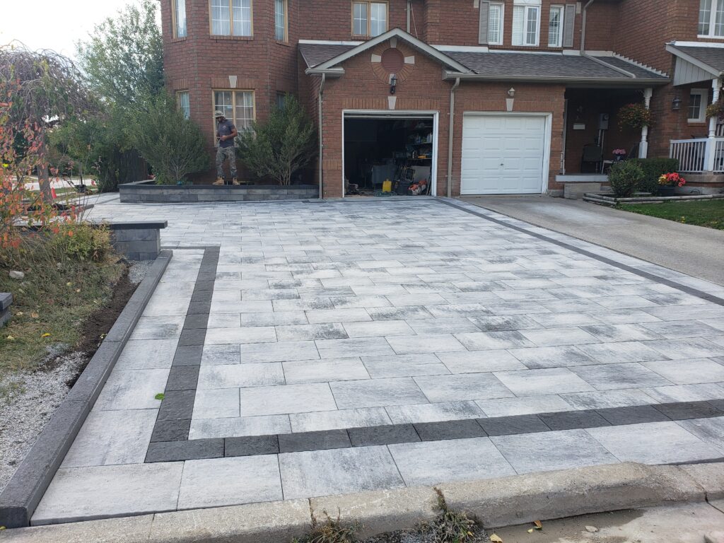 Front driveway installation featuring Oaks Rialto 80mm rectangle pavers in Marble Grey, Unilock Beacon Hill smooth pavers in Midnight Charcoal, and Best Way Stone driveway curbs in Charcoal. Includes Oaks Nueva 150 wall for flower beds. Serving Aurora, Stouffville, East Gwillimbury, Newmarket, Nobleton, King City, Richmond Hill, Vaughan, Toronto, Oakville, Markham, North York, Etobicoke, and the Greater Toronto Area
