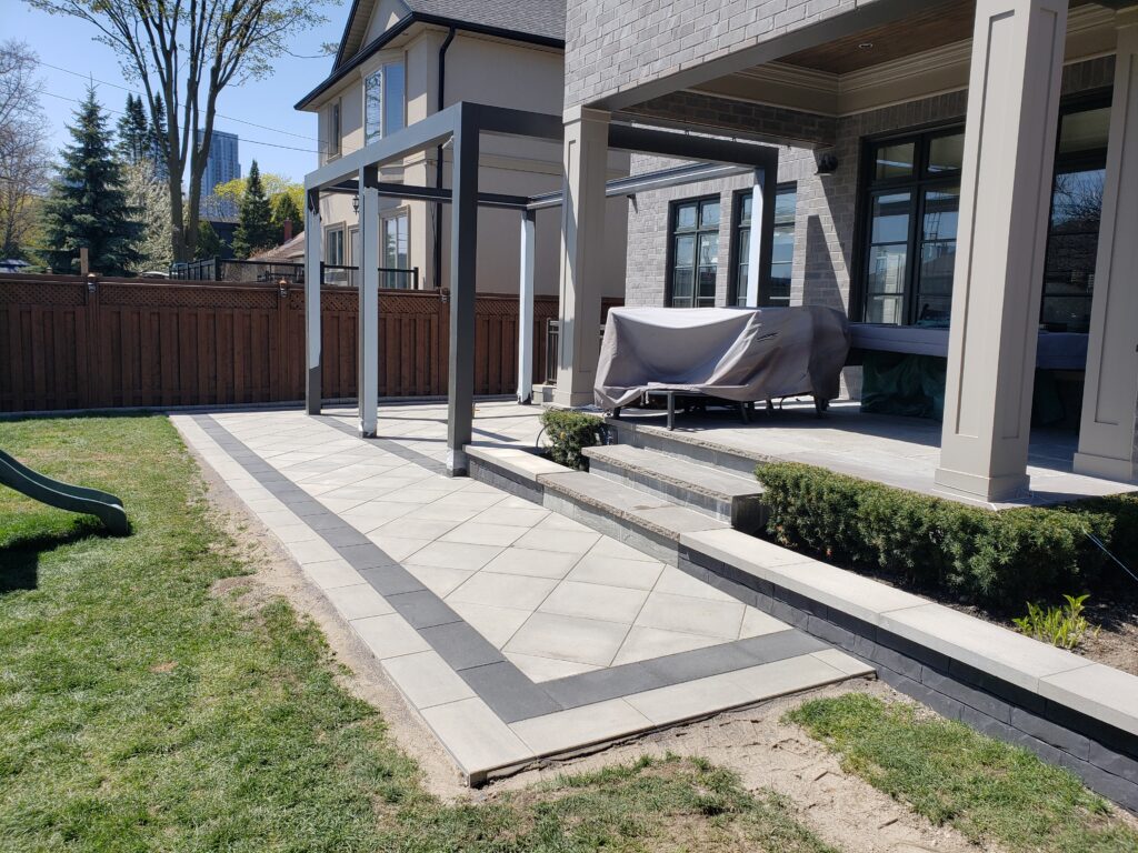 Backyard in Etobicoke featuring Techo-Bloc Para pavers in Greyed Nickel with Onyx Black borders, a diamond pattern, and decorative flower beds. Professional interlocking and landscaping services available in Aurora, Stouffville, Richmond Hill, East Gwillimbury, Newmarket, Nobleton, King City, Mount Albert, and surrounding GTA areas