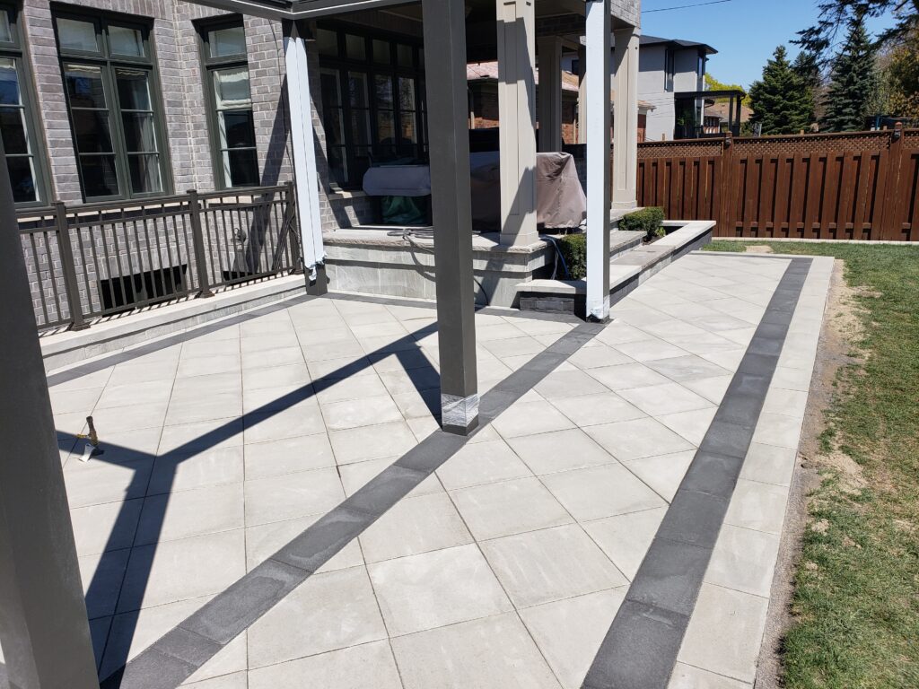 Backyard in Etobicoke featuring Techo-Bloc Para pavers in Greyed Nickel with Onyx borders in a diamond pattern, decorative flower beds, and a buried concrete pad. Serving Aurora, Stouffville, Richmond Hill, East Gwillimbury, Newmarket, Etobicoke, Nobleton, Mount Albert, and King City