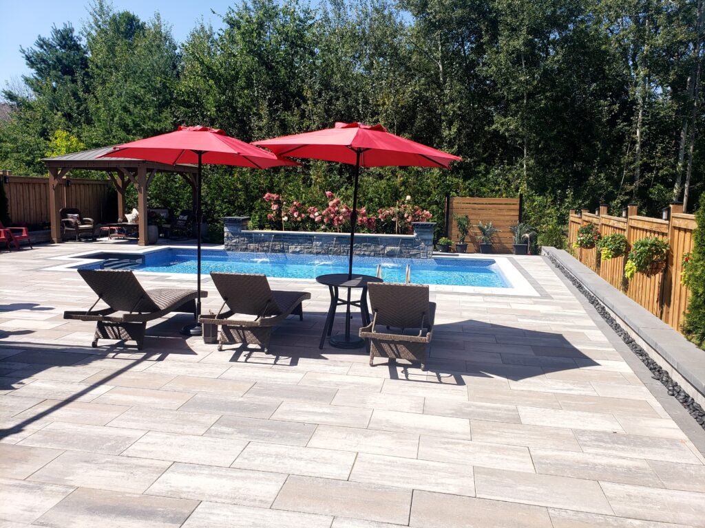 Backyard featuring natural stone pool coping, a waterfall, stone pillars, interlocking pavers, and retaining walls