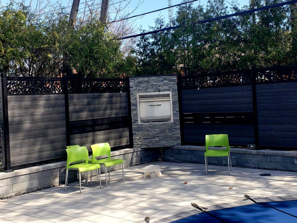 "Custom backyard fire oven built on Oaks Nueva 150 retaining wall, surrounded by natural stone veneers and metal privacy screens, serving Aurora, Newmarket, Stouffville, Richmond Hill, Nobleton, King City, North York, and Vaughan