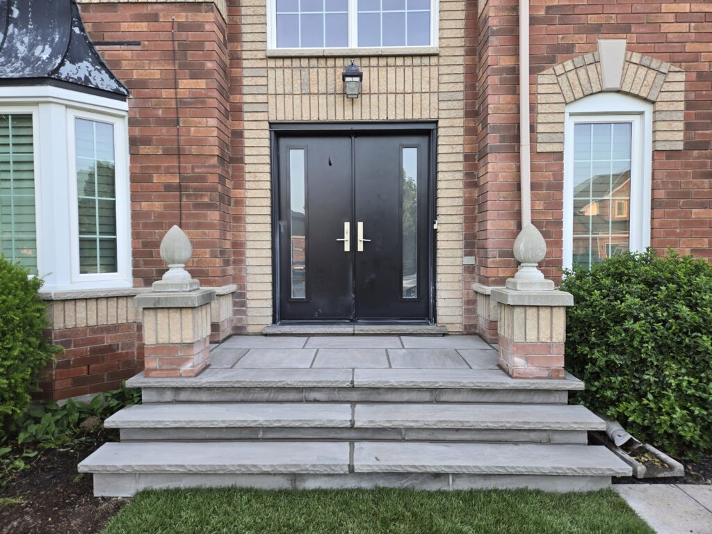 Two custom poured concrete steps with 1 ft deep slate grey coping, rock-faced hand-chiseled edges, and slate grey flagstone on porch and risers, expertly crafted in Aurora, Richmond Hill, Vaughan and North York