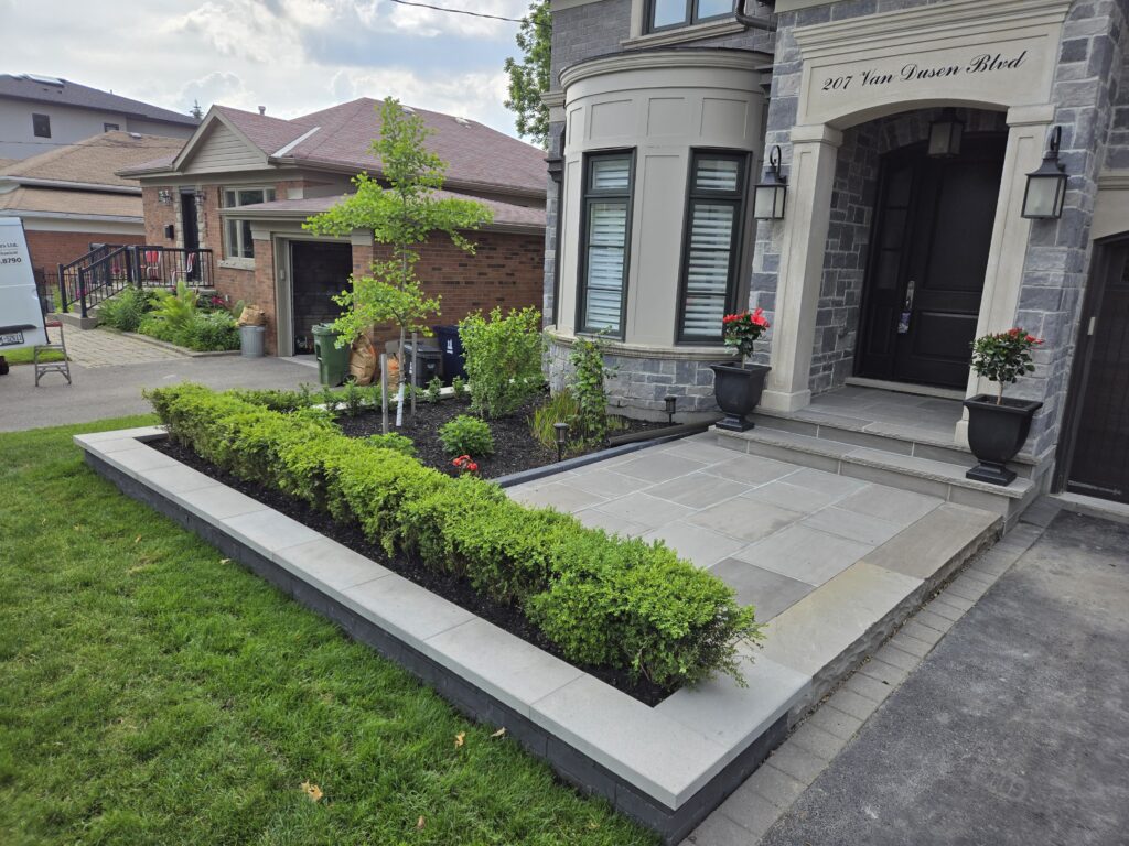 Custom flower bed wall with Techo Bloc Brandon Onyx blocks and Raffinato Greyed Nickel caps, featuring natural stone slate grey steps and a poured concrete pad with slate grey flagstone and curbs in Etobicoke, Aurora, Richmond Hill and North York