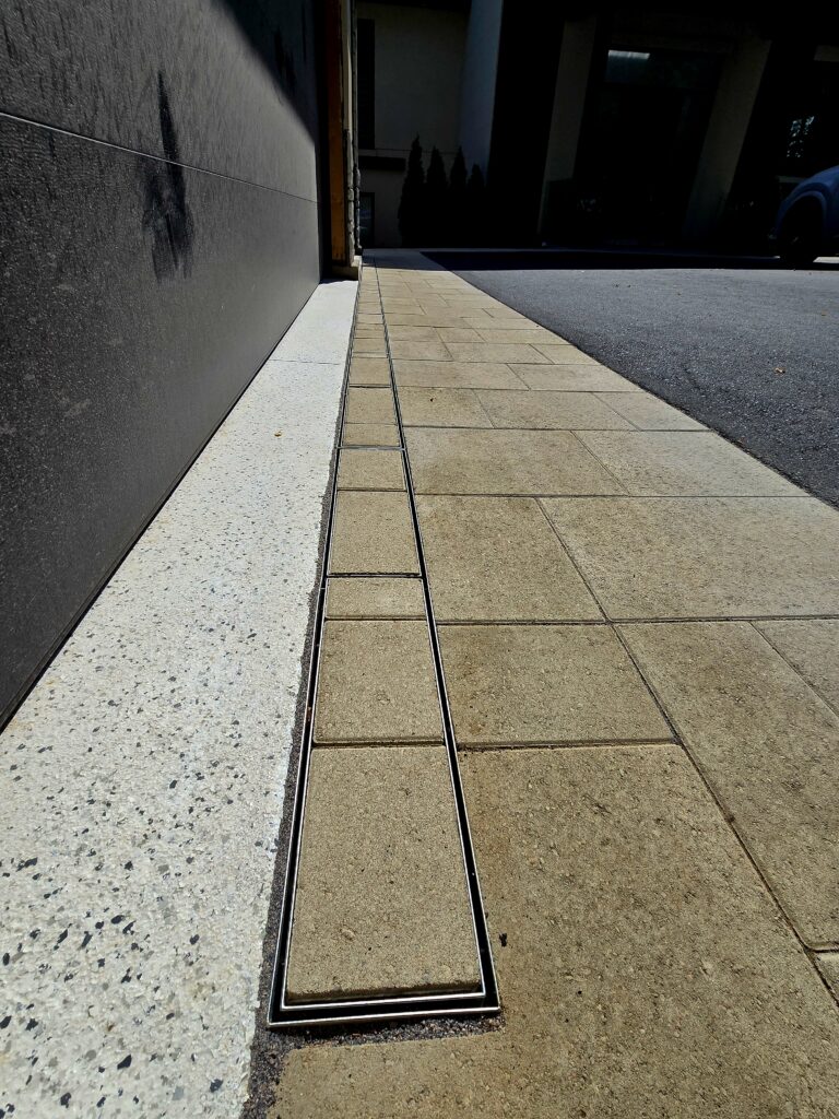 Amber Beige interlocking pavers with integrated French drain by the garage for smooth water drainage with asphalt driveway installed by Premier Masonry in Newmarket