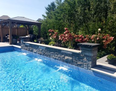 Handcrafted natural stone waterfall made from tiger stripe ledge rock, featuring Venetian crema copings and granite-capped stone pillars