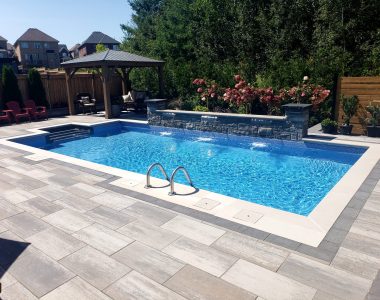 Backyard oasis transformation featuring interlocking pavers, retaining walls, hand-chiseled stone pillars, and custom waterfall