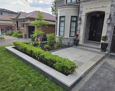 Flower bed wall with Techo Bloc Brandon Onyx blocks, Raffinato greyed nickel caps, natural stone slate grey steps, and a custom poured concrete pad with slate grey flagstone and curbs