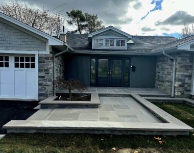 Heated two-level front landing with Slate Grey flagstone, flower beds built with Oaks Modan wall in Champagne color, and topped with Slate Grey rock-faced natural stone coping