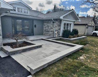 Heated two-level front landing with Slate Grey flagstone, flower beds built with Oaks Modan wall in Champagne color, and topped with Slate Grey rock-faced natural stone coping